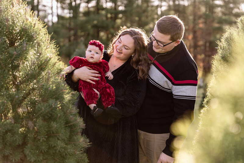 Parents holding their baby on a Christmas tree farm.
