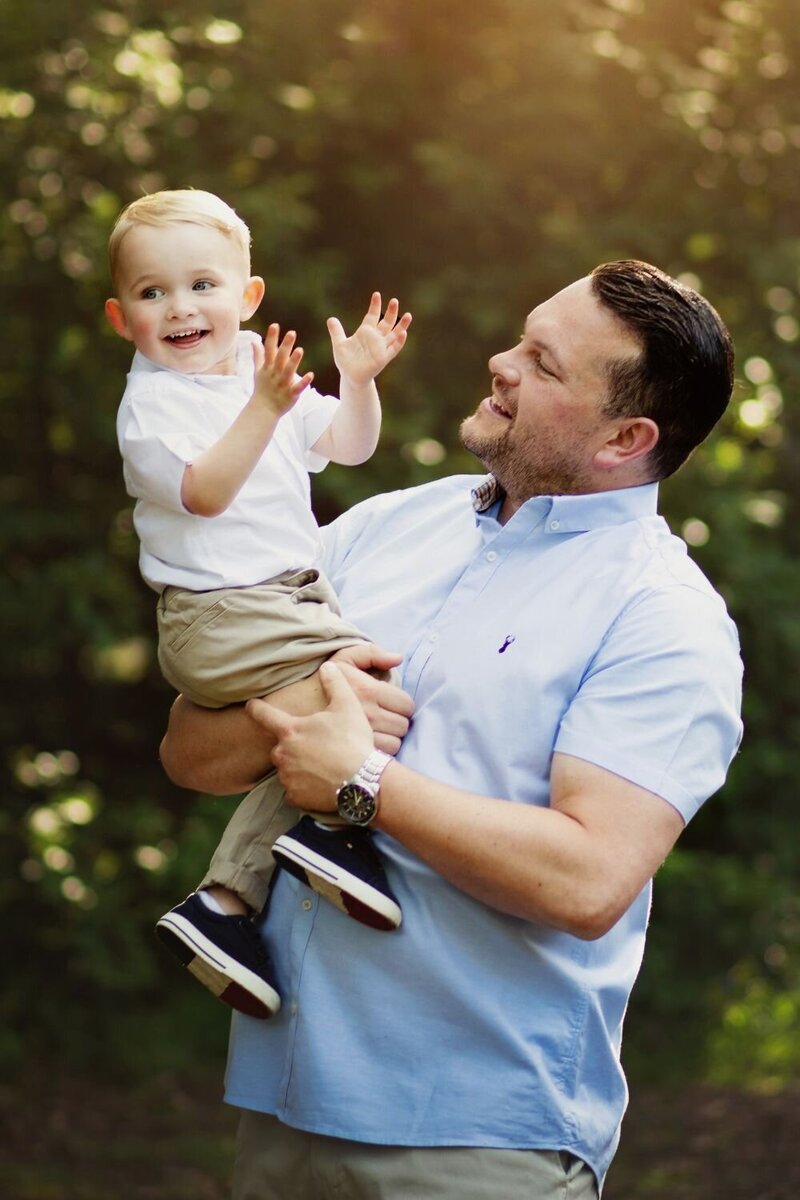 Father holds up his son as he claps  and smiles