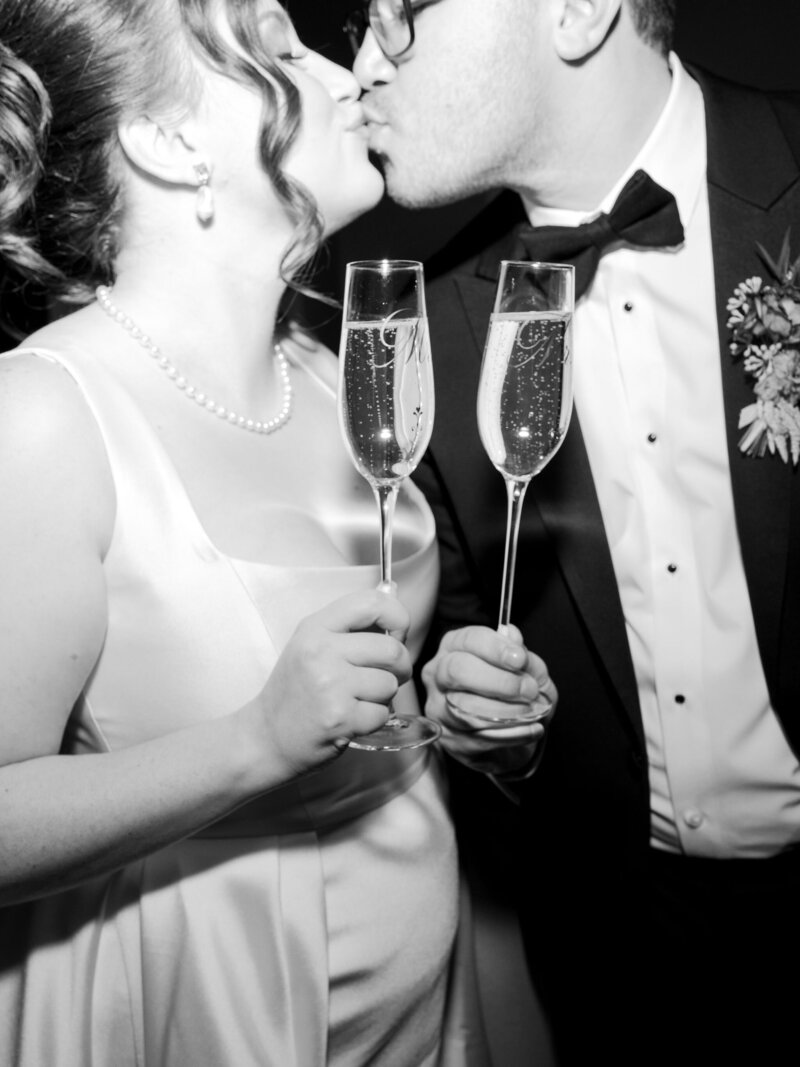 A black and white wedding photo of a couple kissing during the champagne toast at their wedding reception.