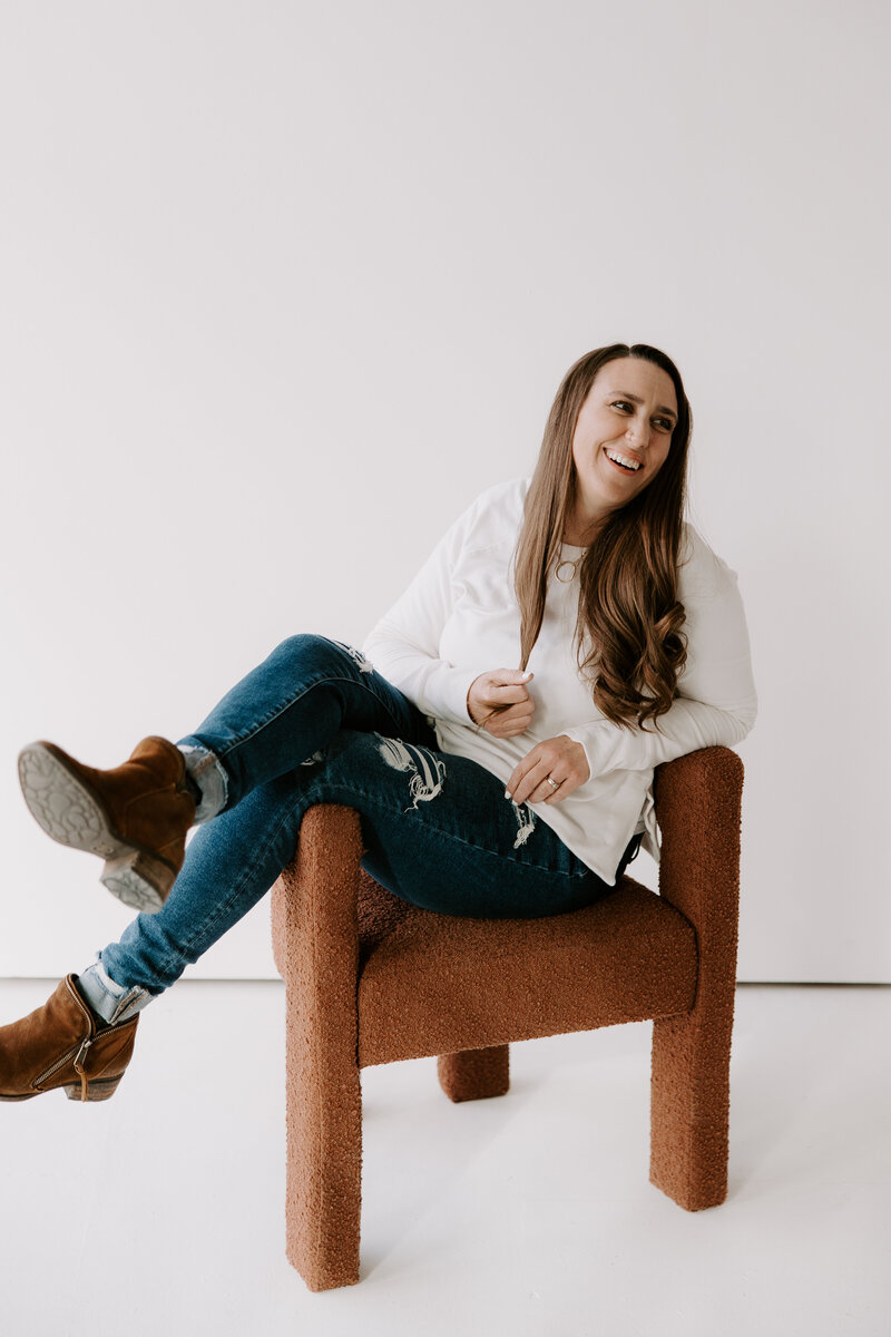 A Denver branding photography and strategy coach sitting in a chair looking off to the side as she thinks about branding photos and brand strategy.