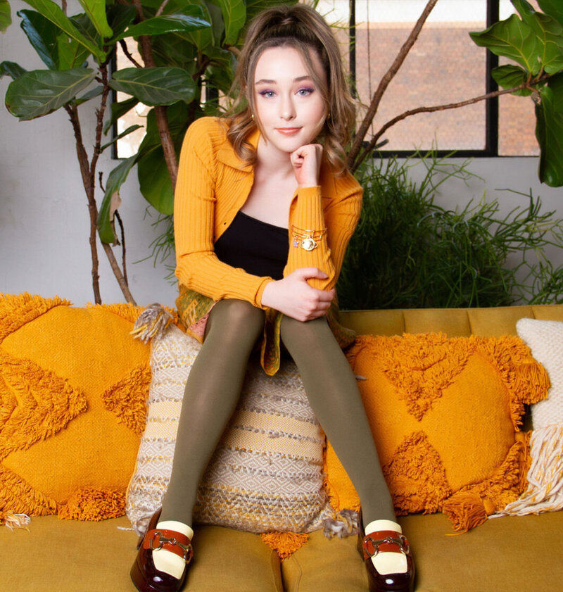 Tween branding portrait sitting with chin resting on hand wearing orange shirt on couch with orange pillows