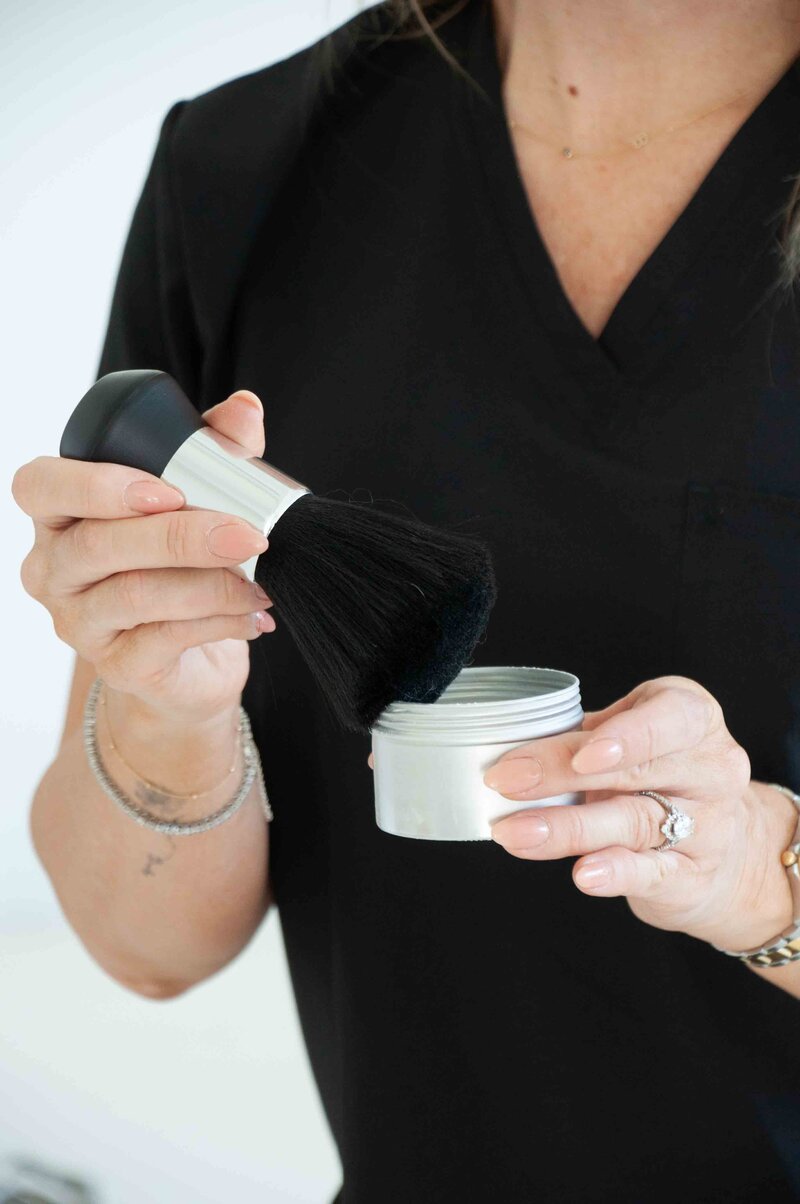 The proffesional of our skin care expert wielding a coarse black brush and magic powders for the perfect final touch to your whitening spray procedure