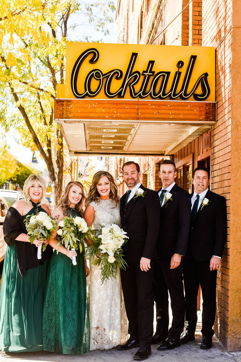 Downtown Flagstaff wedding party bridal smiling at camera Cocktails sign brick wall