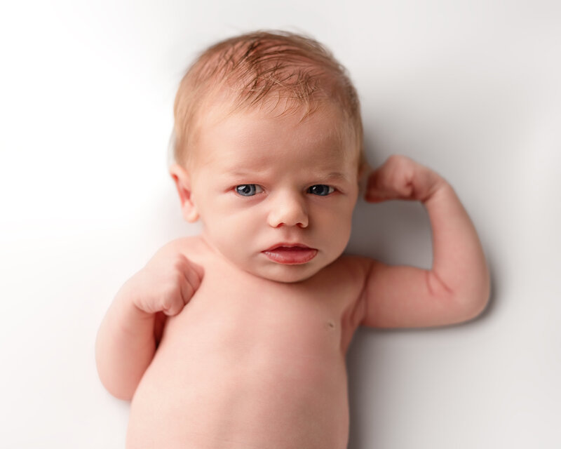 A striking personality portrait of a newborn flexing with confidence—captured in studio lighting to highlight strength and character.