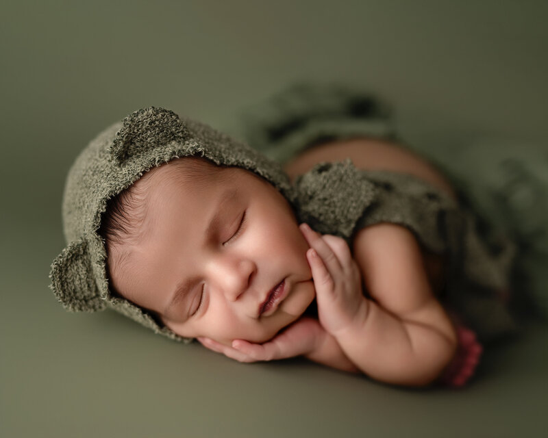 Gentle side pose with a forest-toned bear bonnet – newborn boy in serene slumber.
