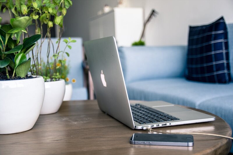 Mac book open on brown coffee table next to iphone with blue counch in the background