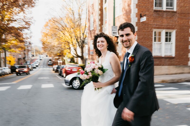 bride and groom walking on a cross walk in the city to get totheir Richmond wedding venues location with autumn trees lining the street and brick buildings in the distance