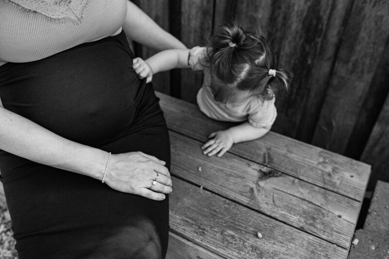 Zwangerschapsfoto buiten mama met oudste dochter. Dochter raakt de zwangere buik aan. 