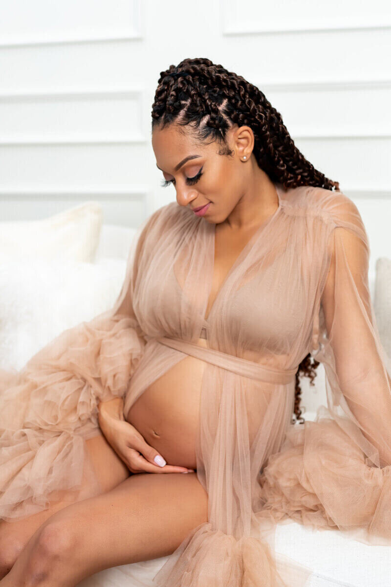 Black pregnant woman sititng on couch holding belly in brown goddess dress
