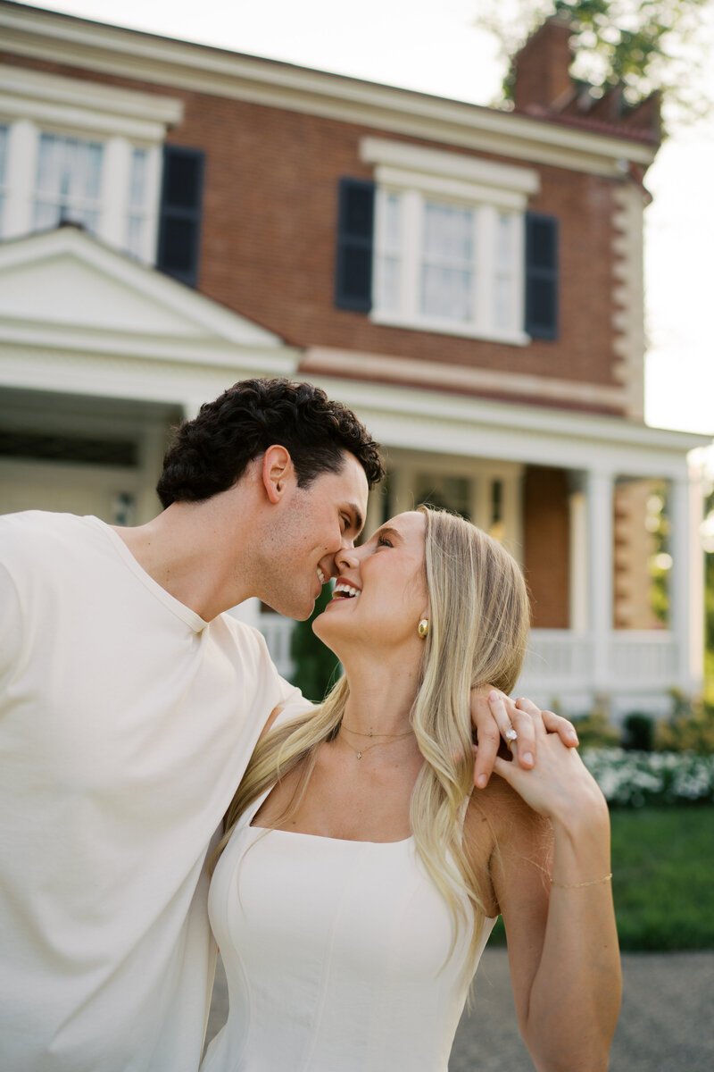 A couple holding hands in front of Ravenswood Mansion laughing wearing white t-shirts.