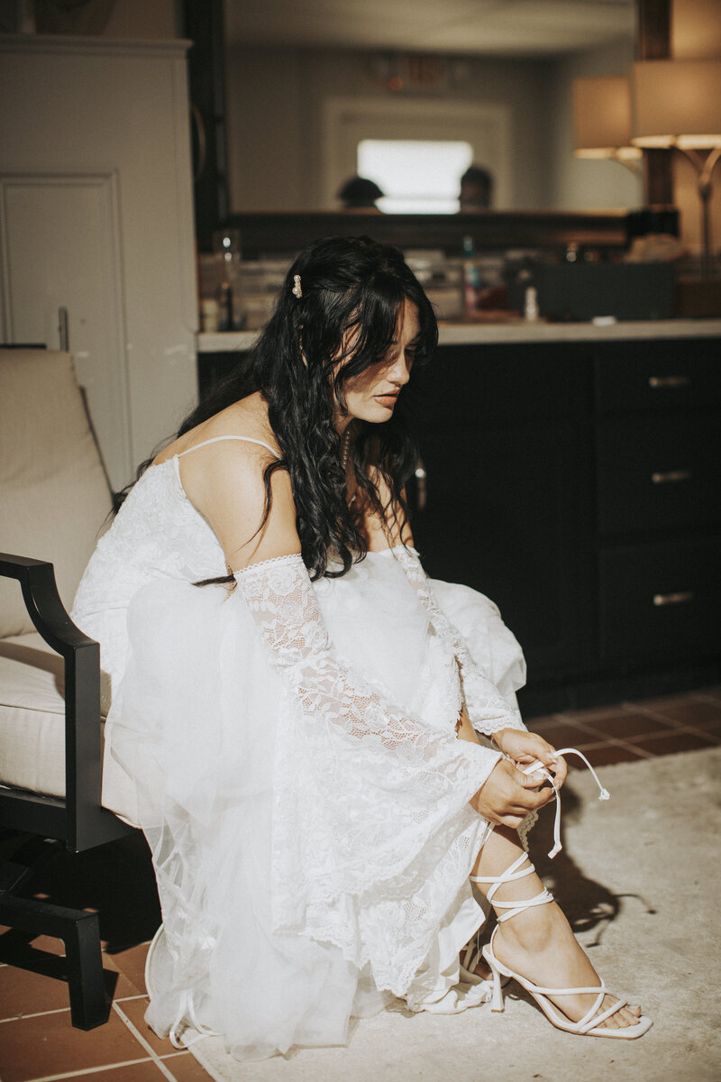 Bride adjusting her dress in front of a mirror while getting ready in a softly lit bridal suite