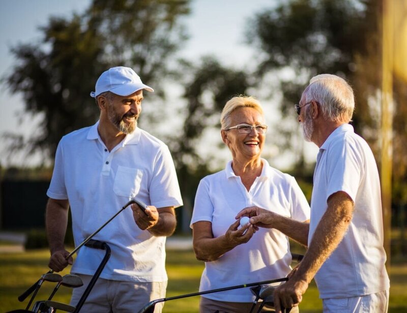 An elderly man happily passing a golf ball to an elderly woman.
