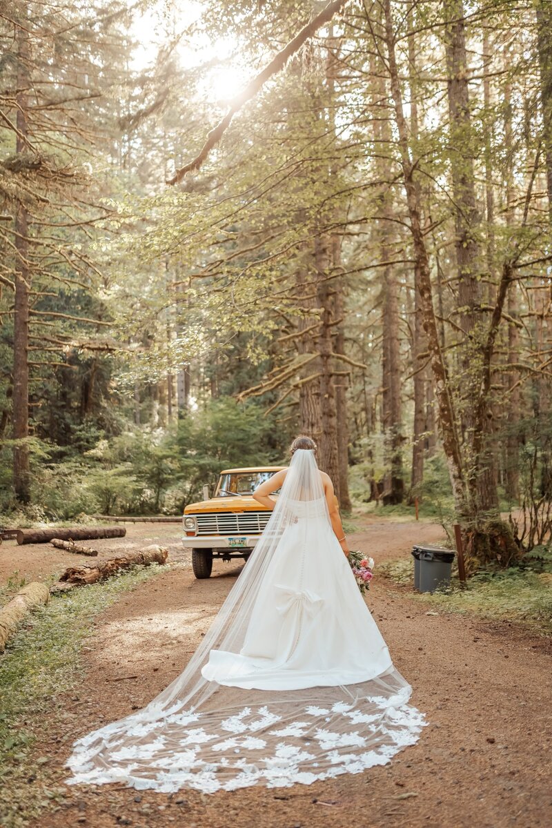 real bride wearing custom lace bridal veil with new and vintage heirloom lace posing in the forest with a vintage truck