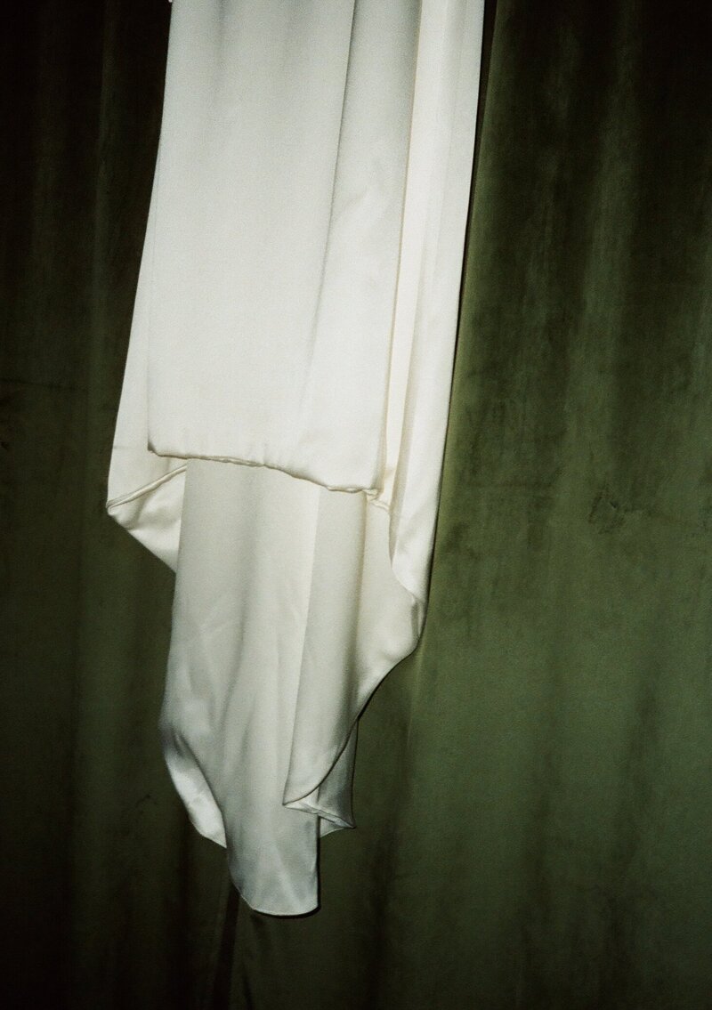 Wedding gown elegantly drapes against a rich green backdrop