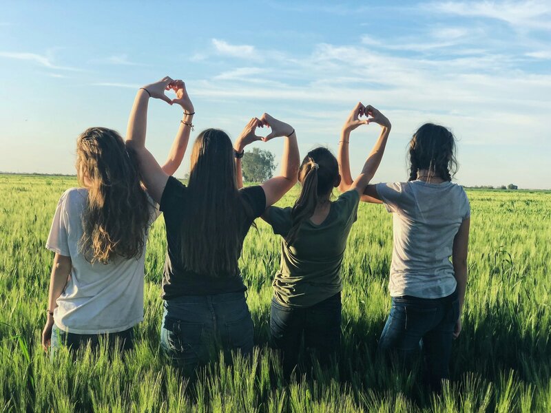 Group of women standing in a field making a chan of hearts with their hands