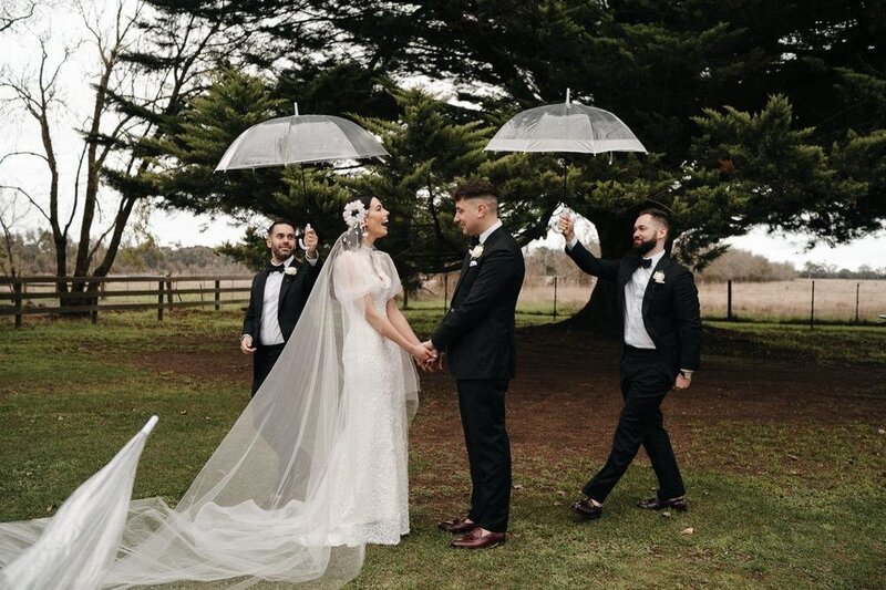 couple being brought umbrellas at wet wedding at Cadella Park