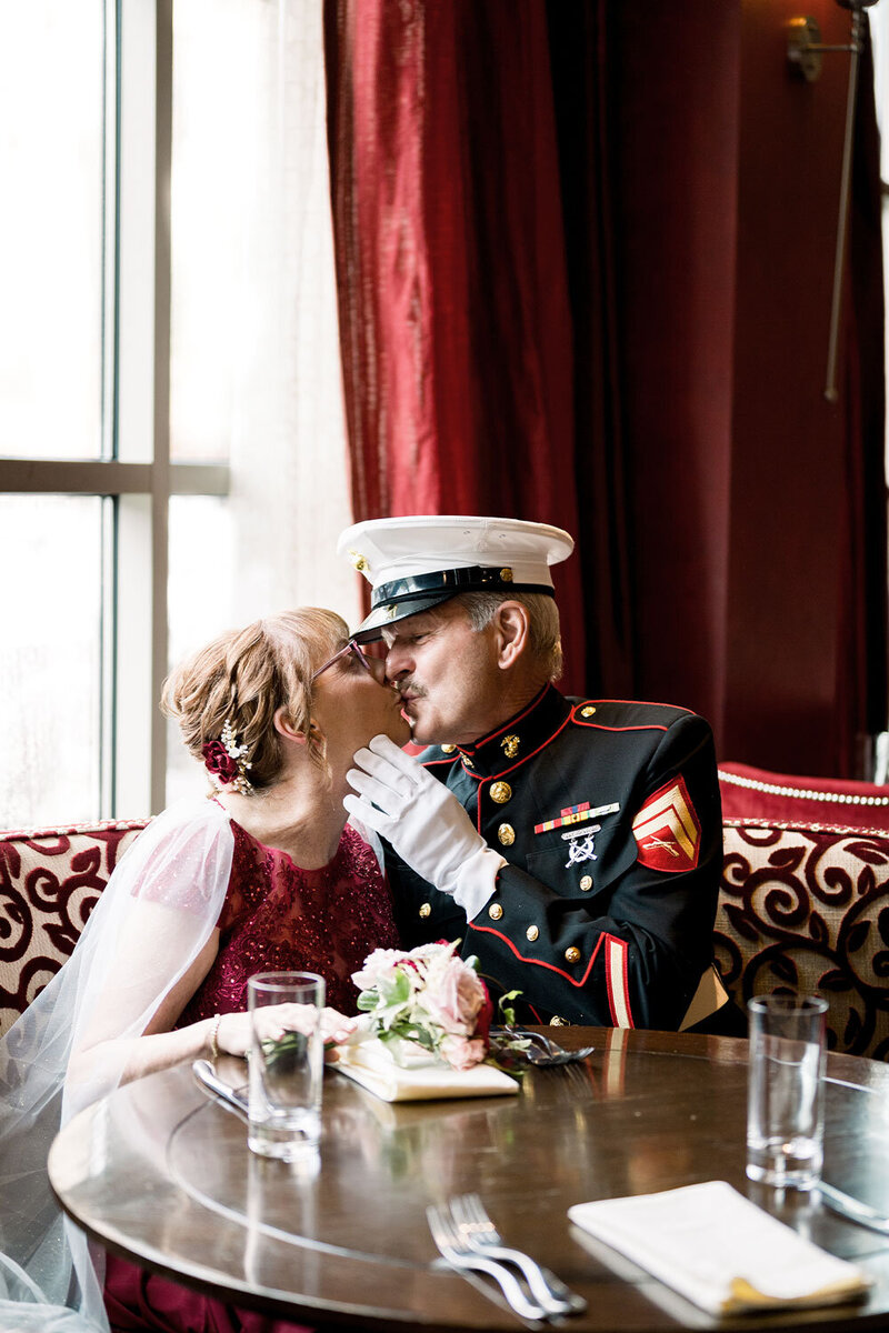 Bride and Marine kissing in restaurant booth for their anniversary celebration.