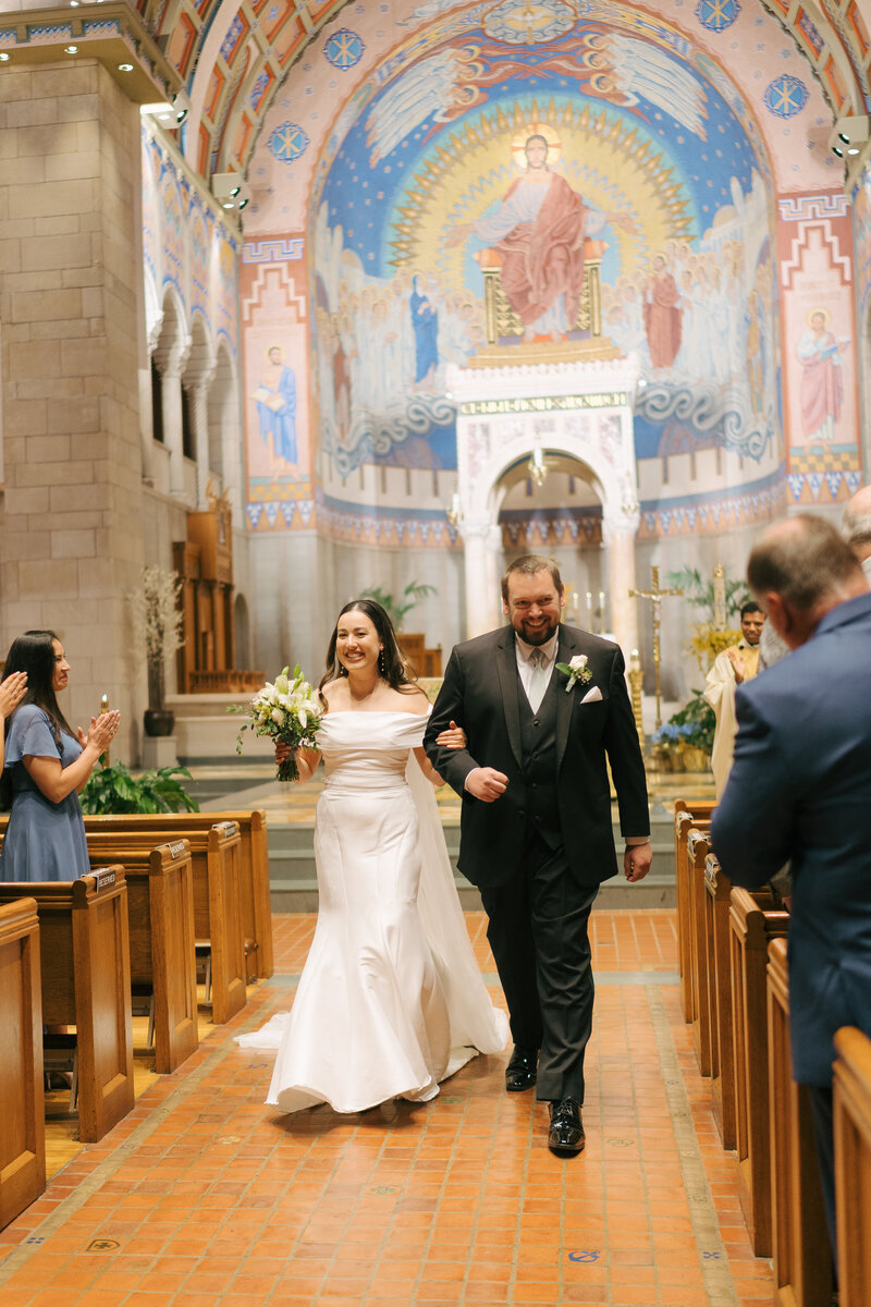 A bride and a groom holding hands smiling walking out of their cathedral wedding venue in Nashville, Tennessee.