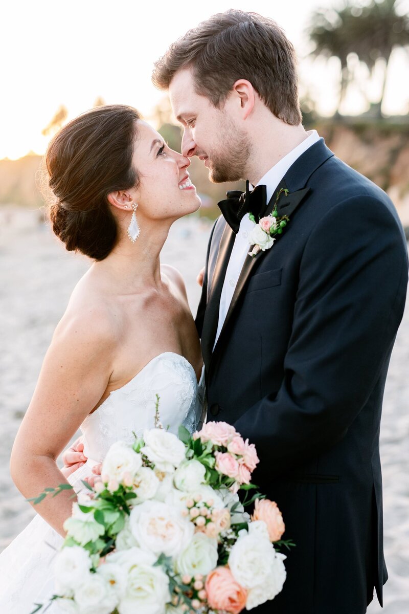 Bride and groom smile nose to nose on the beach on their wedding day