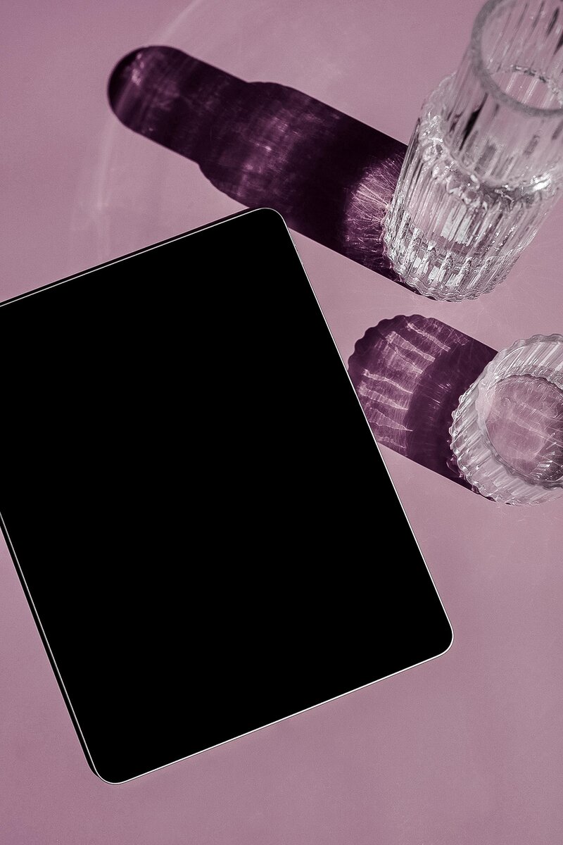Vaso de agua de cristal  y tablet sobre fondo morado.