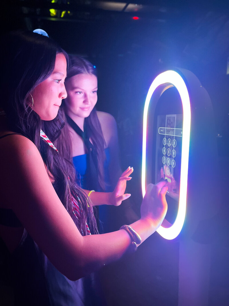 Two girls are getting their photos texted to them from the photo booth.