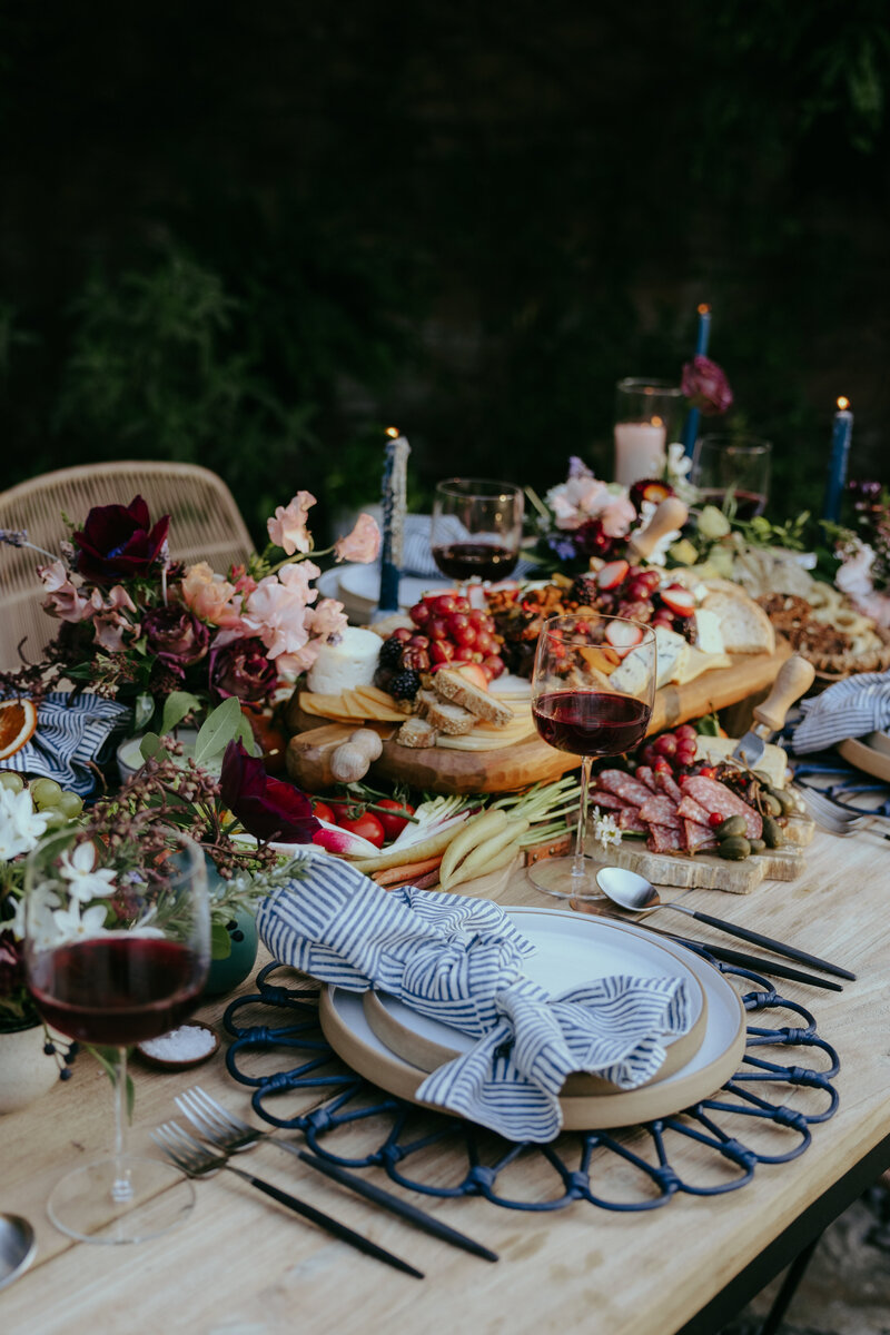 Wedding table setting featuring a light wood table, striped blue and white napkins, and colorful flowers and vegetables for the table decor.