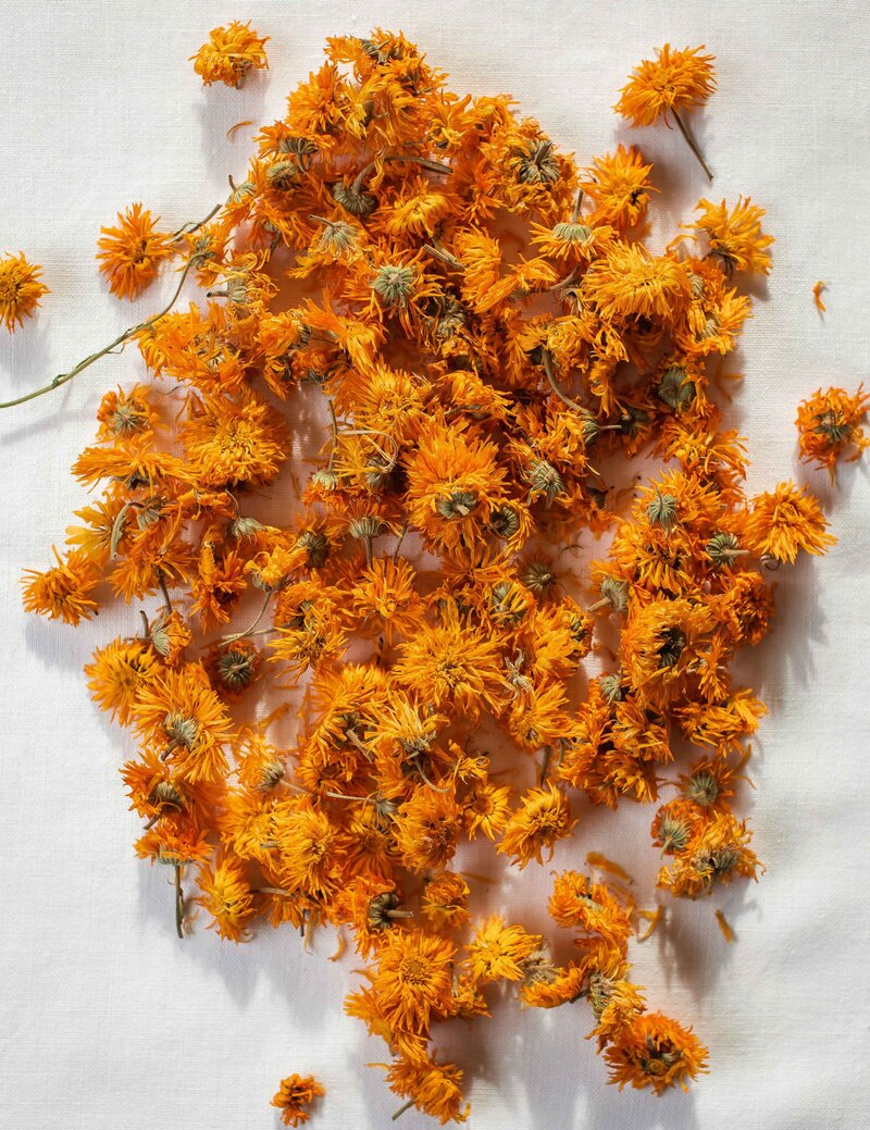 A linen cloth covered in bright orange dried calendula blossoms.