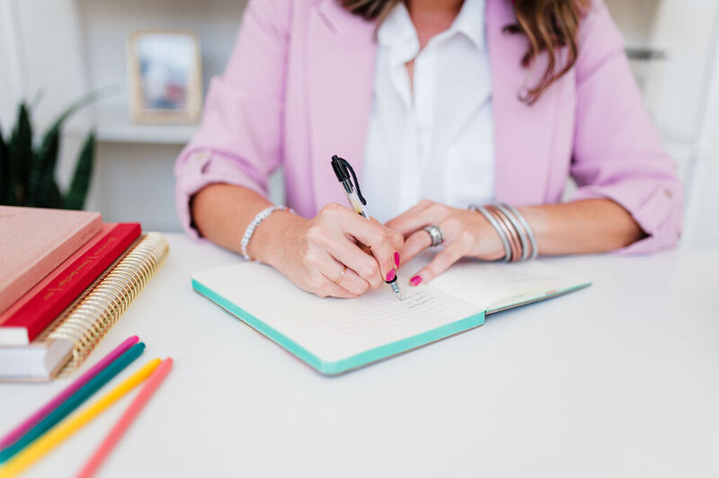 woman sitting on desk holding a stack of books