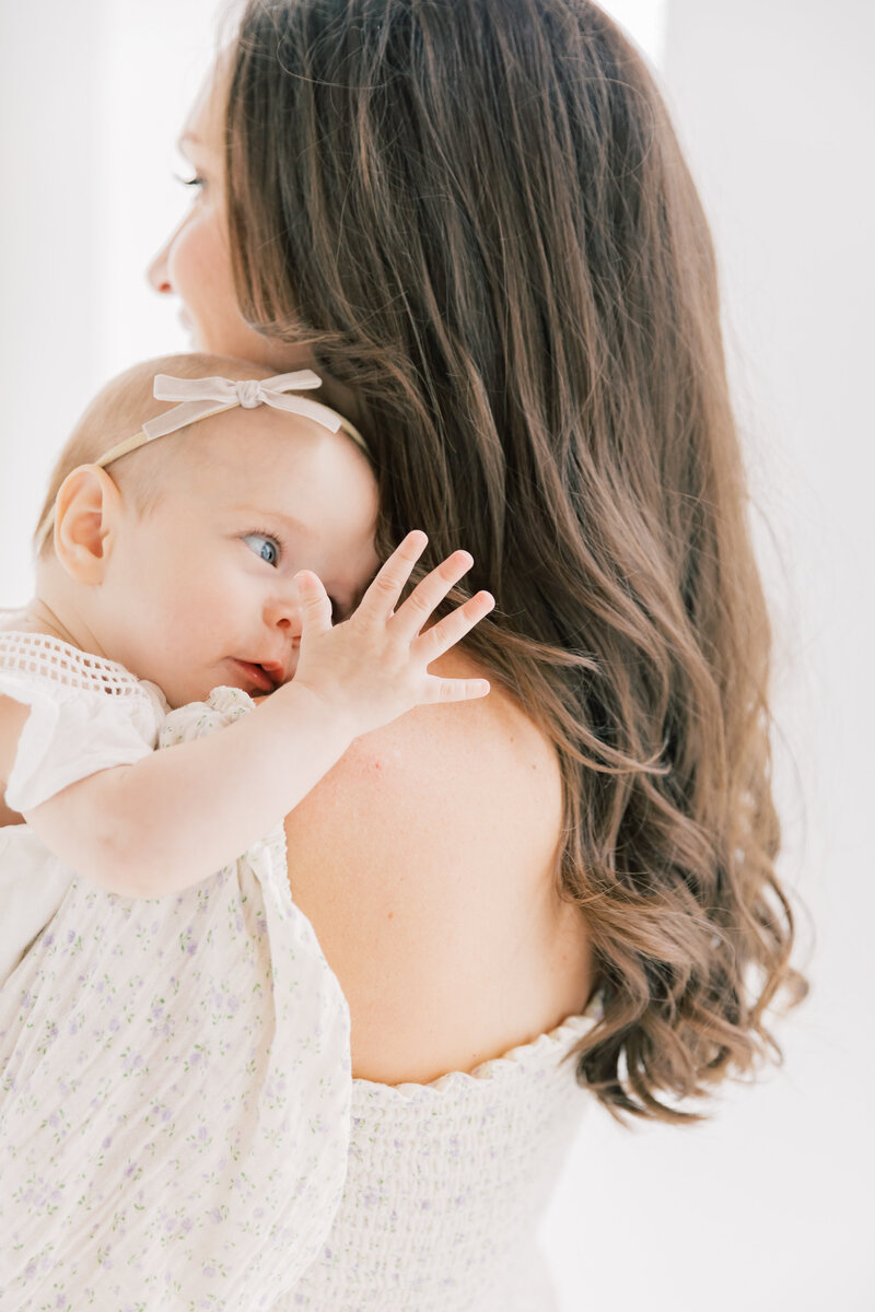 An infant girl examines her hand while laying on mom's shoulder