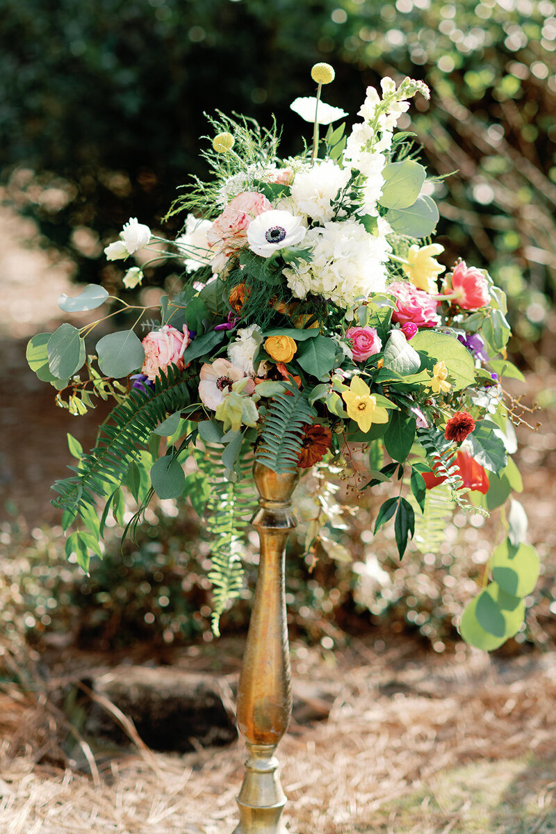 Colorful floral arrangement in brass tall planter sitting outside 