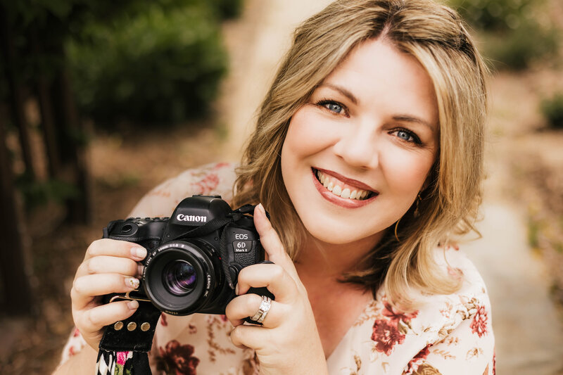 Up close portrait of woman in a floral shirt smiling and holding a large camera