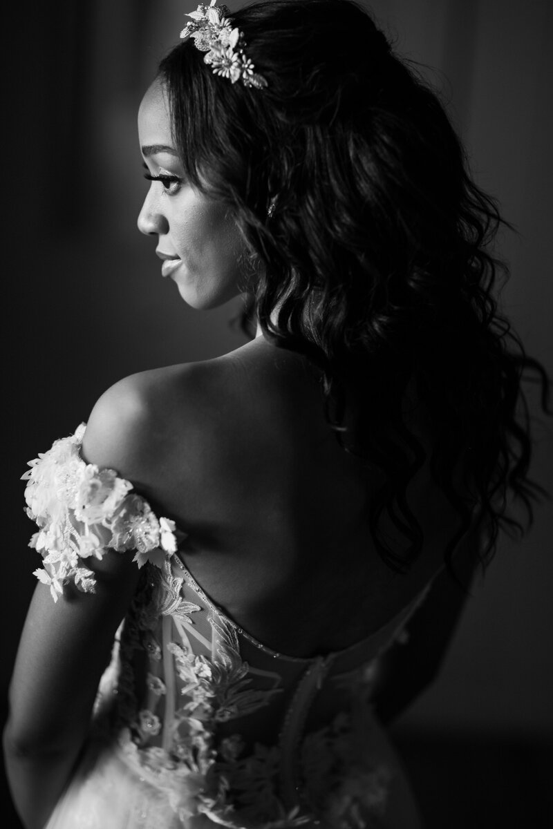 Black bride in a delicate off shoulder wedding gown gracefully smiles over her shoulder