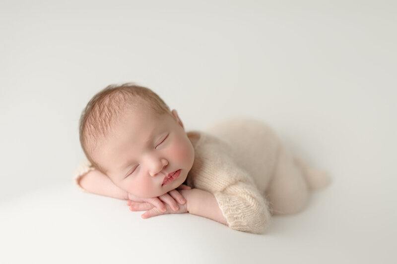 Peaceful newborn portrait with baby girl posed with head on hands in soft cream tones – Paris, Ontario.