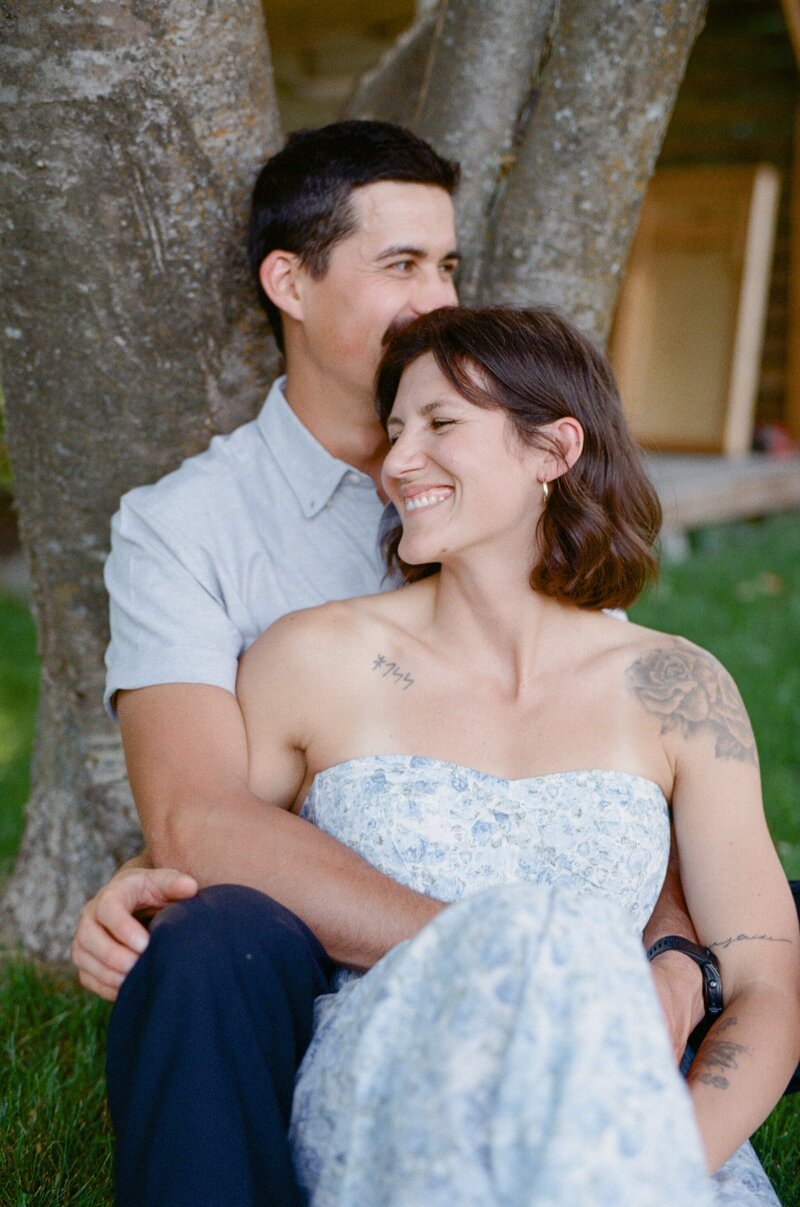film photo of a couple laughing and holding each other in the backyard beside an old tree