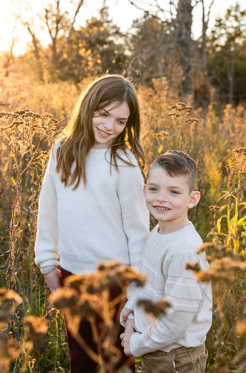 Brother and sister standing in a field during golden hour. 