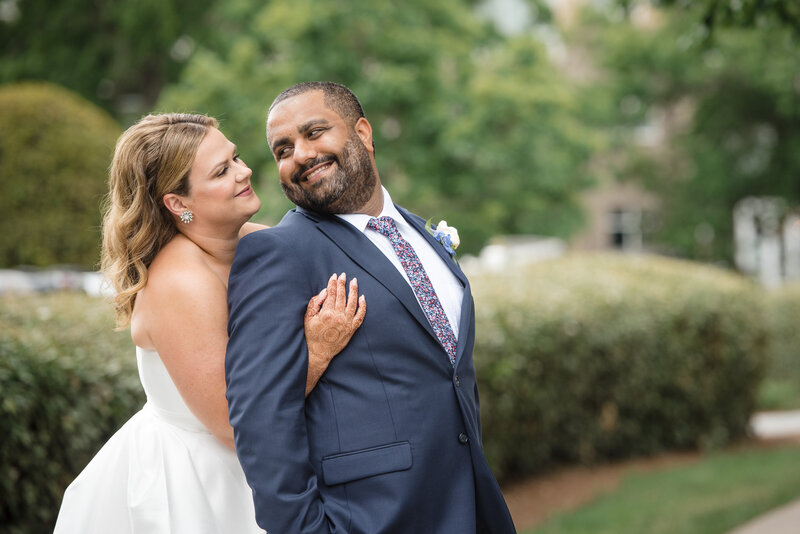 Interracial wedding couple portrait at Le Méridien Charlotte with bride in white gown embracing groom in navy suit. Captured by DeLong Photography, expert Charlotte Indian wedding photographers.