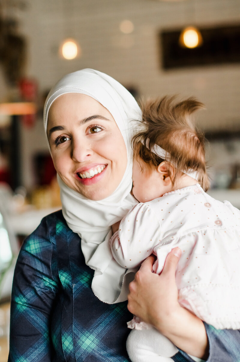 Fitness hijabi coach Hanan posing with a smile while holding a baby girl