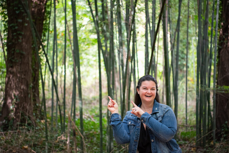 A woman pointing up and smiling in a bamboo forest.