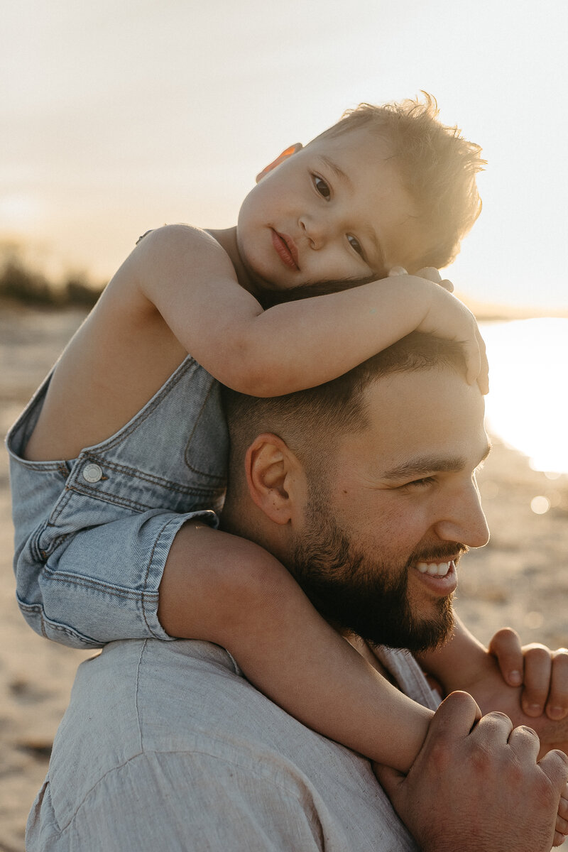 Little boy sitting on dad's shoulders and hugging him on the beach