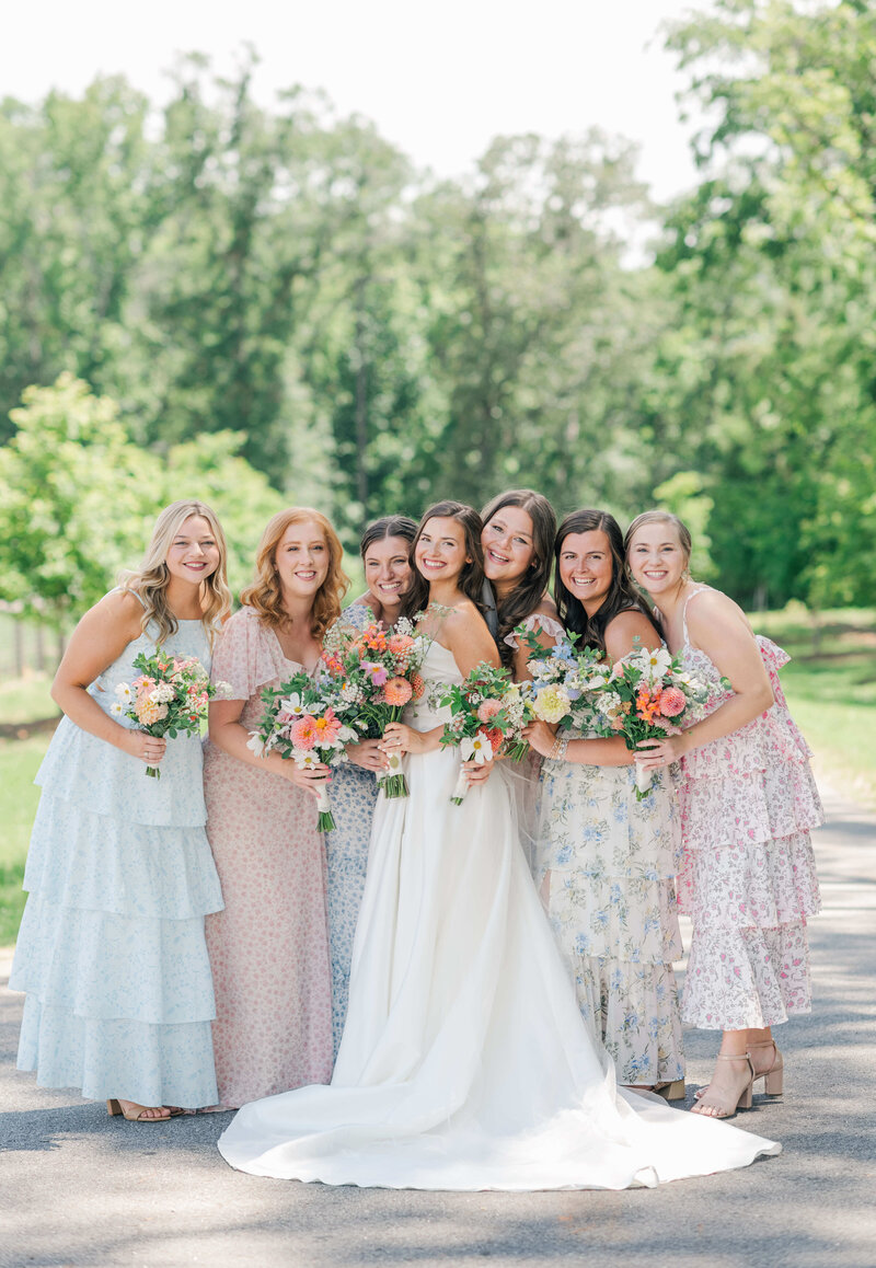 Bride surrounded by bridesmaids and bouquets smiling att he caemera