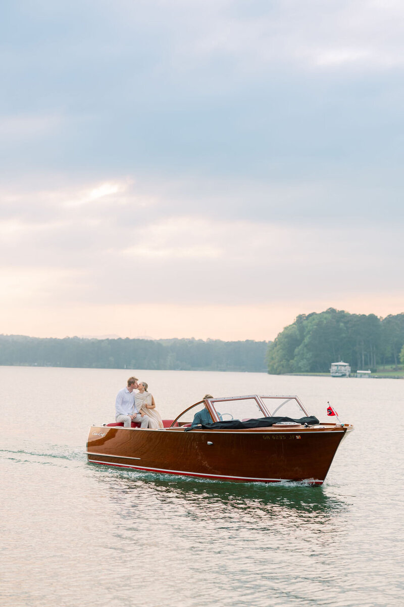 Bride and groom kiss on back of vintage boat on Lake Lanier