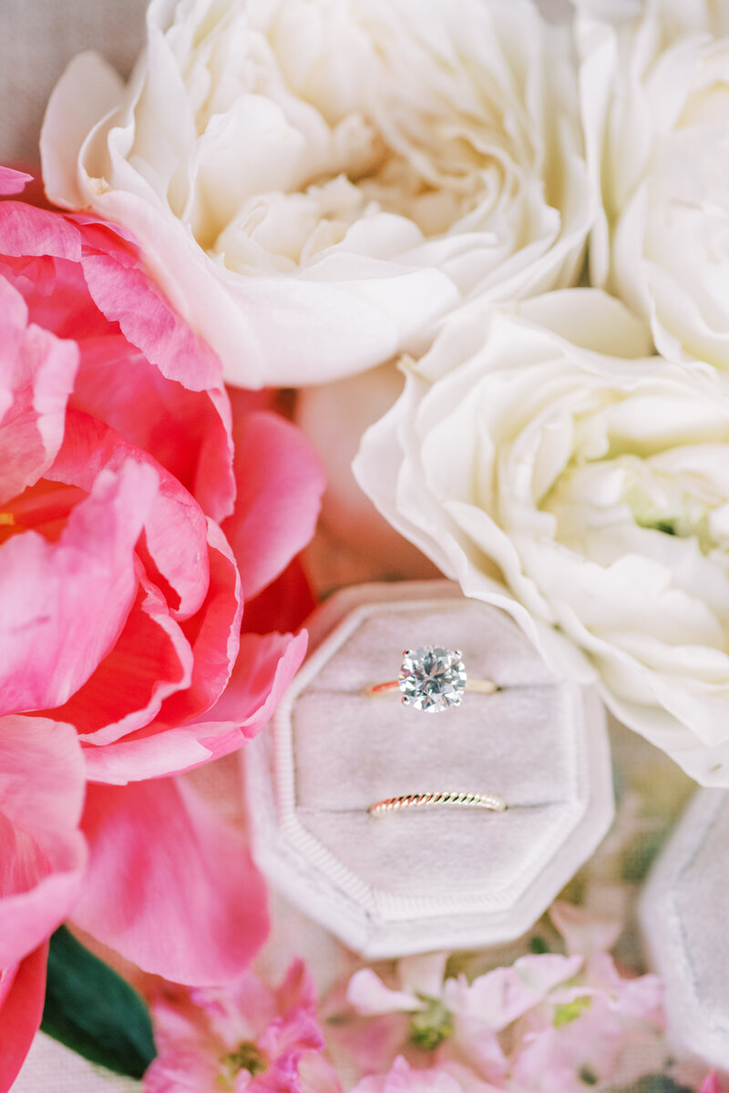 Close up image of wedding rings in a light pink ring box surrounded by pink and white flowers