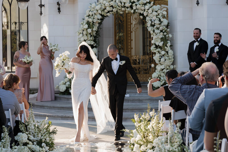 Bride and groom exiting their ceremony under a lavish floral arch, photographed by TM Photos, a T&M wedding team specializing in cinematic celebrations and intimate portraits in Sacramento CA.