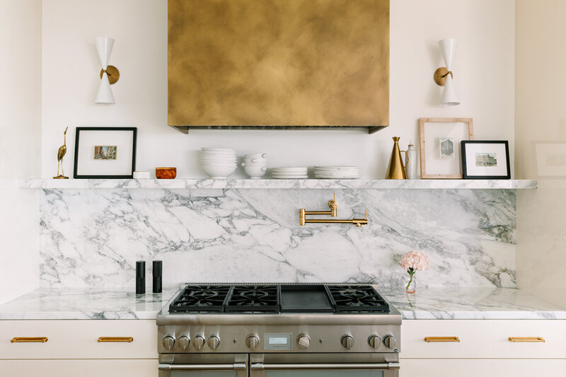 Kitchen with cream cabinets, brass hood, and calcatta marble