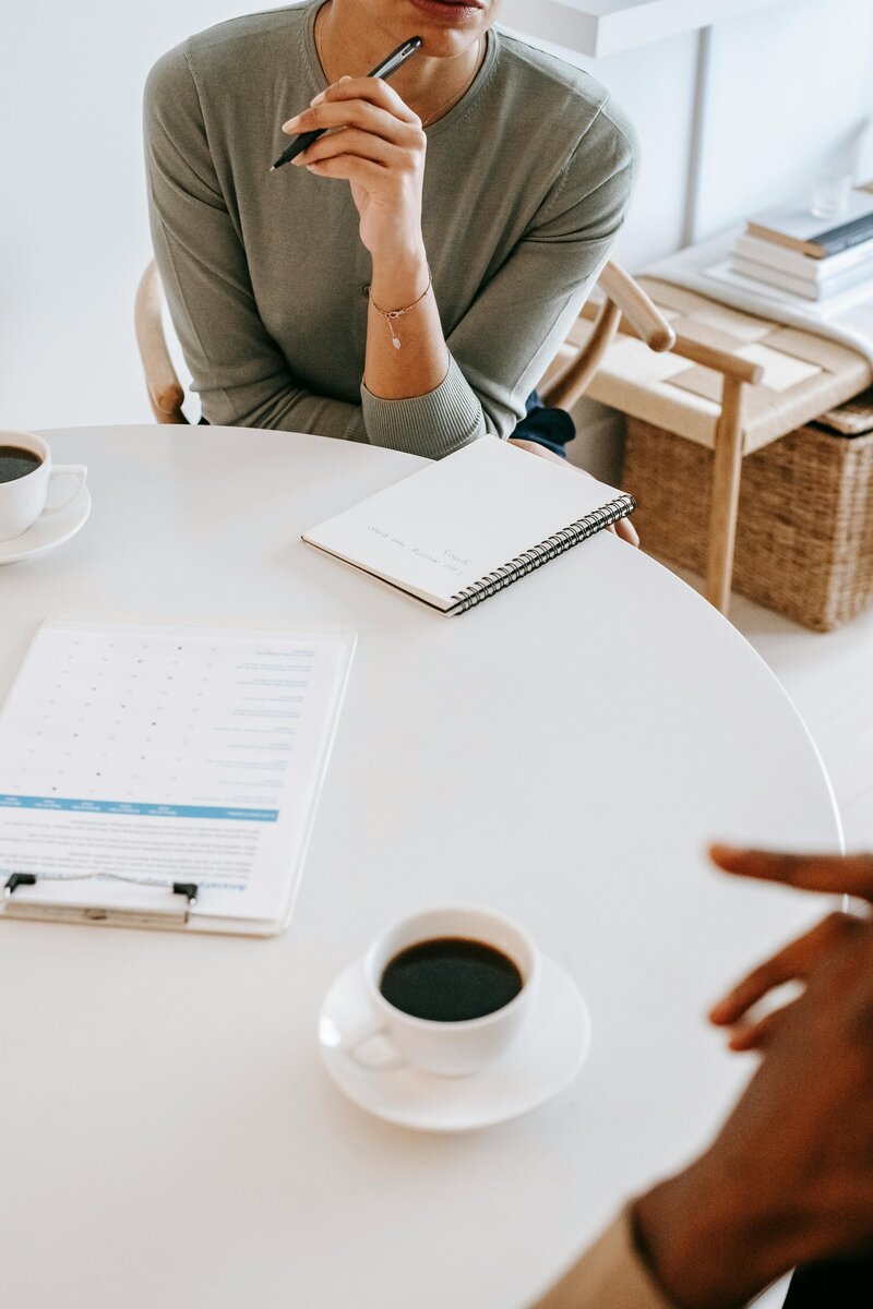 Two people in a therapy session at a table with notebooks, coffee, and paperwork, suggesting collaboration and open communication.