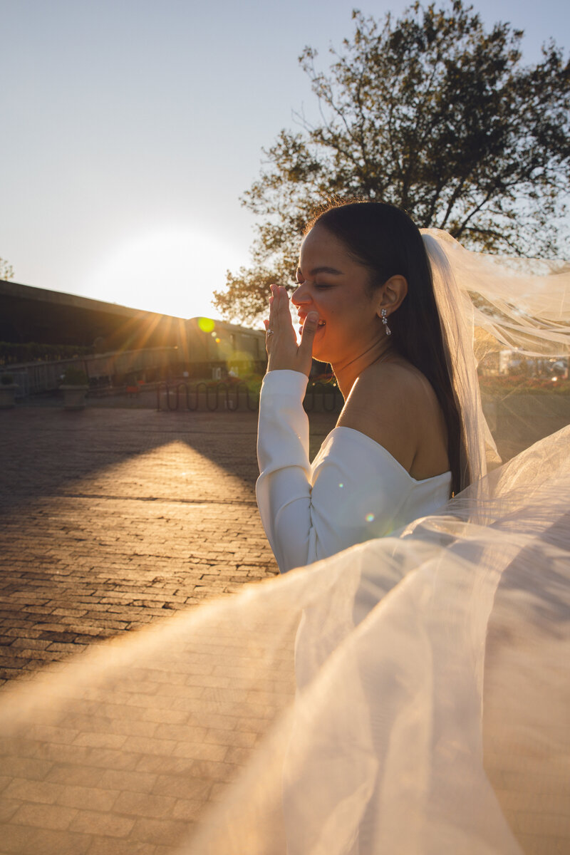 Bride laughing in off-the-shoulder dress at sunset, veil blowing in the breeze during Philadelphia wedding