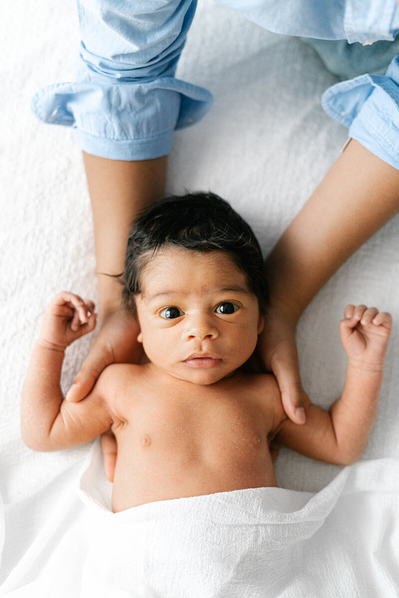 older baby looking at camera with brother hands on baby