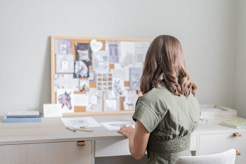 A stationery designer at her desk working on sketches while being photographed by Madalyn Yates Creative.