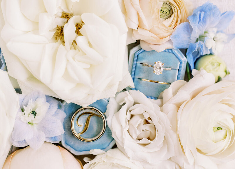 Wedding rings on a light blue velvet box surrounded by white roses
