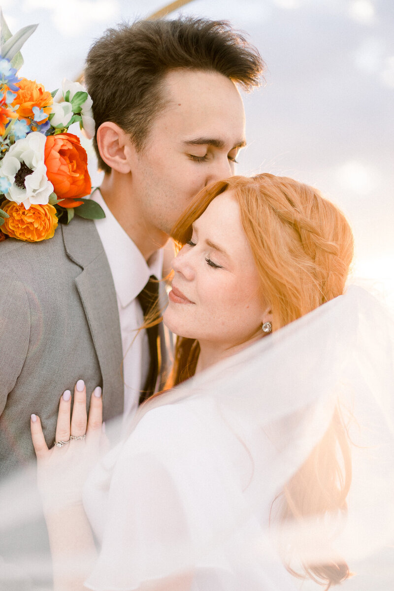 groom kissing bride on side of head while bride is slighly smiling, looking peaceful taken by leavenworth photographer